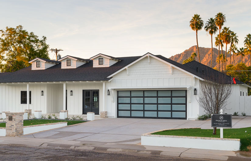 modern landscaped new construction home with blue sky and puffy white clouds. Covered front porch with three car garage